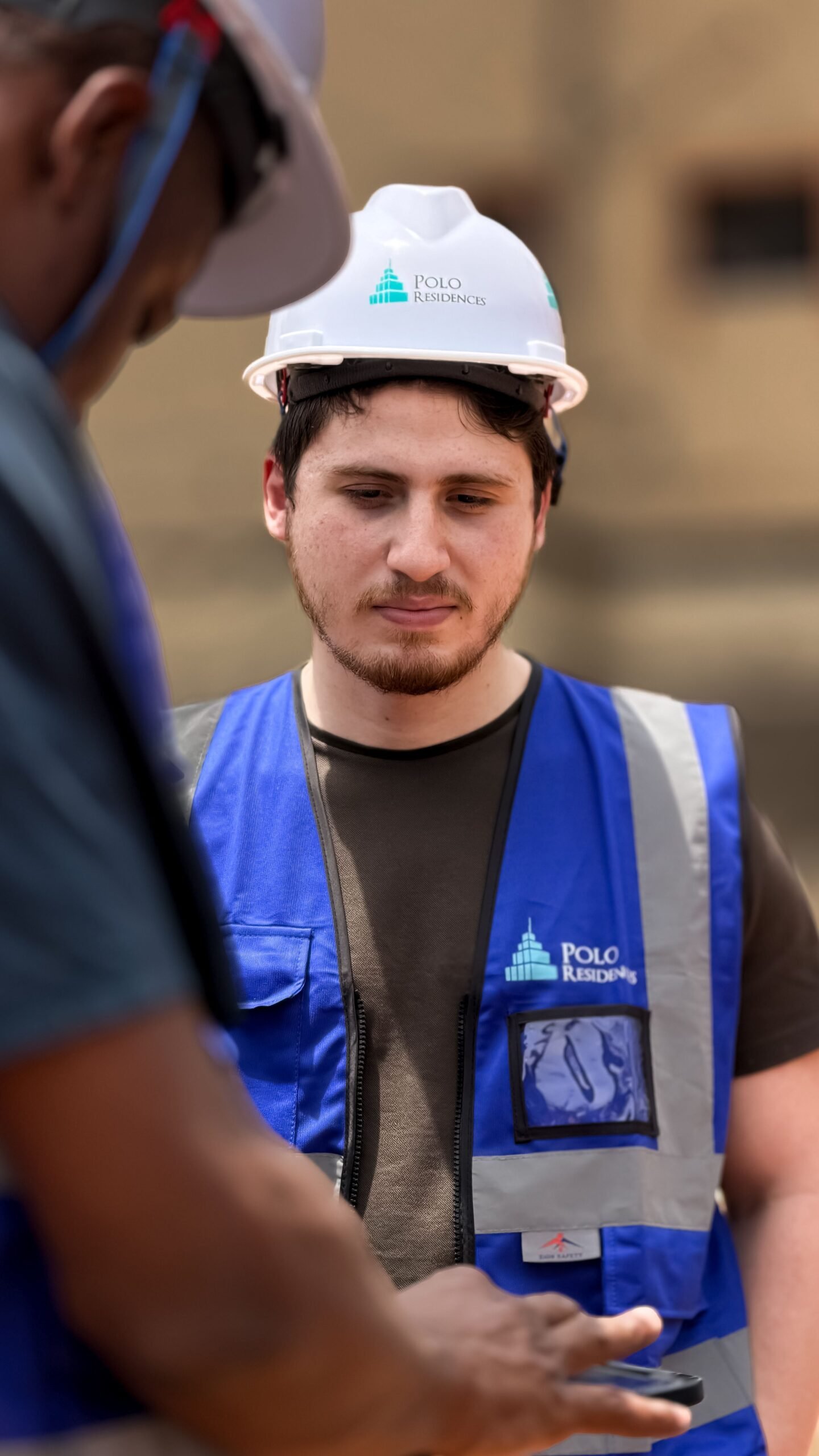 Construction workers engage in discussion outdoors wearing protective gear and blue vests.