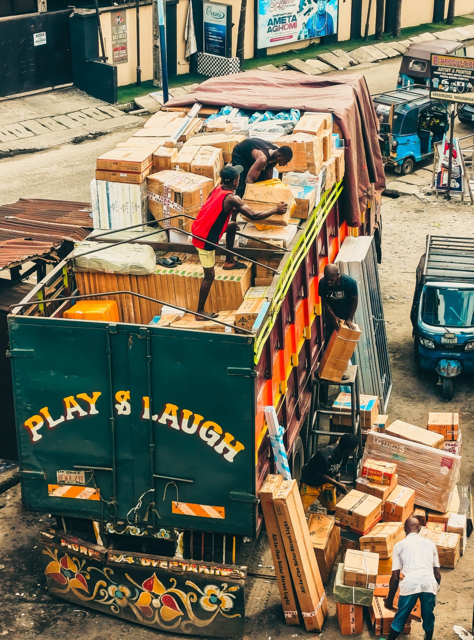 Workers load a vibrant truck with boxes in a busy urban environment, showcasing teamwork and logistics.